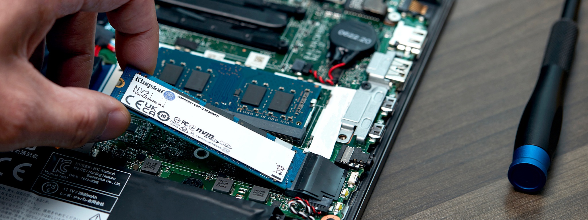 A close-up on a hand installing Kingston NV2 SSD in a laptop