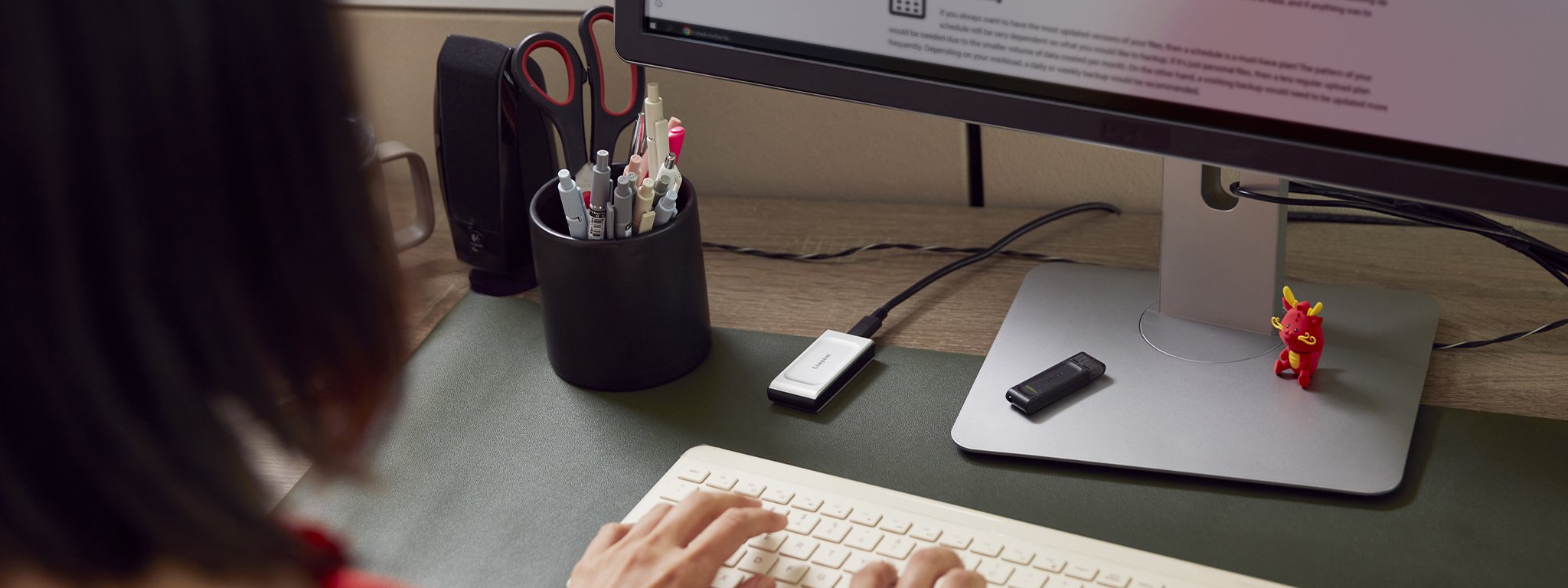 a woman typing on a keyboard with Kingston XS2000 external SSD plugged into her PC