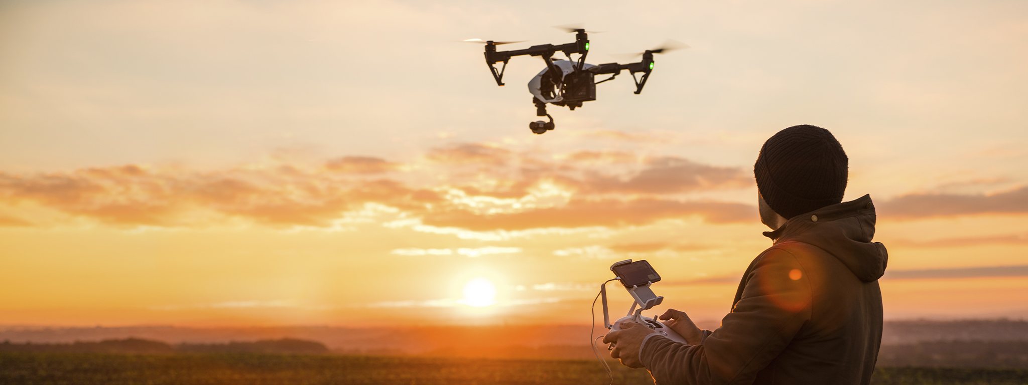 un homme manipulant un drone avec une télécommande au coucher du soleil
