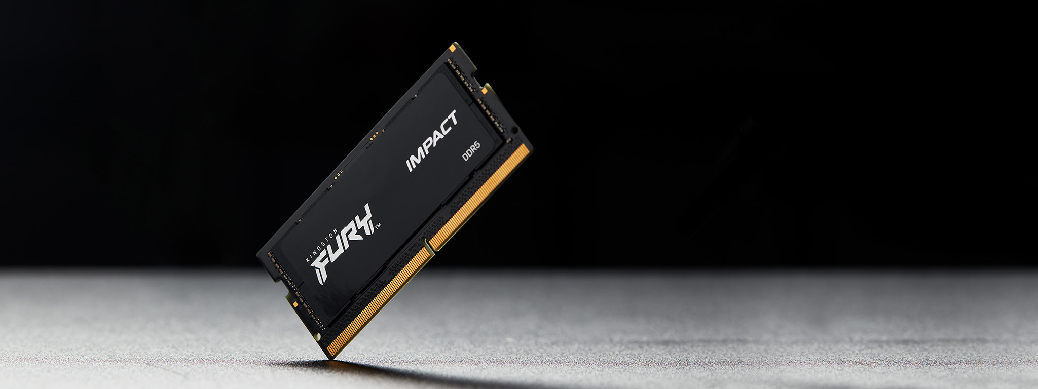 Модуль памяти Kingston FURY Impact DDR5 SODIMM, стоящий вертикально в углу на серой поверхности с черным горизонтом