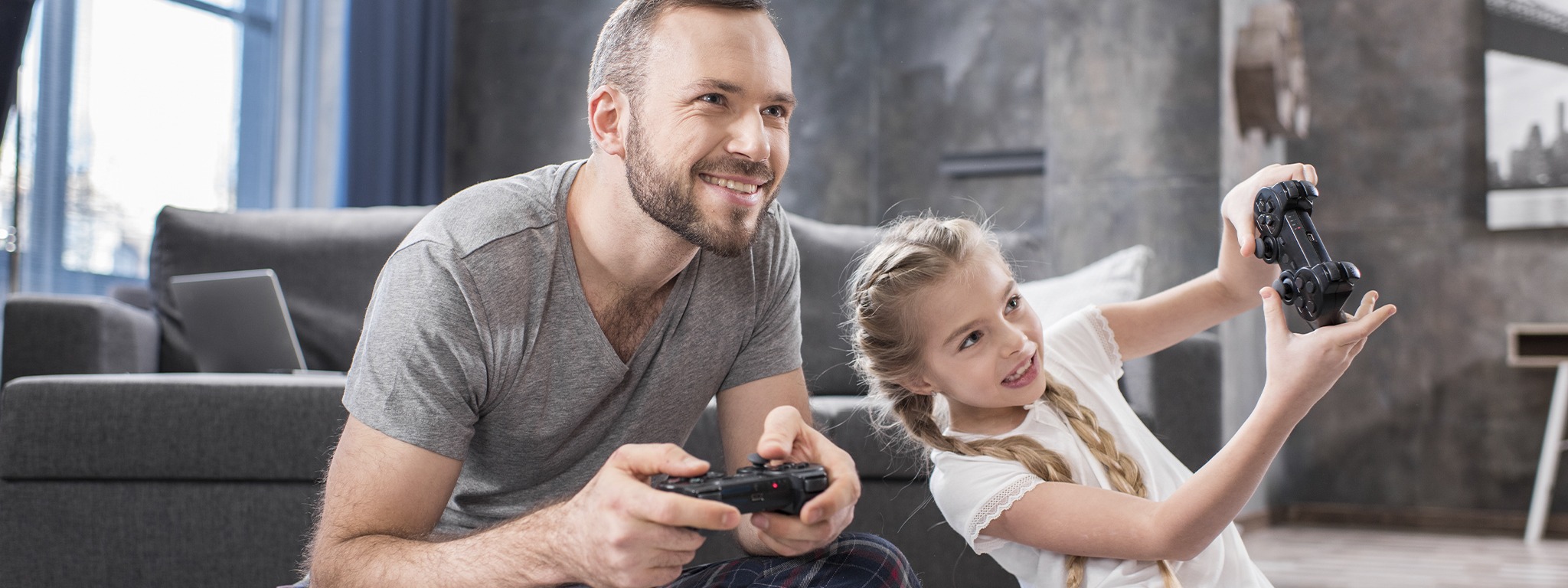 un padre con su hija, sentados en la alfombra de su hogar sumergidos en videojuegos