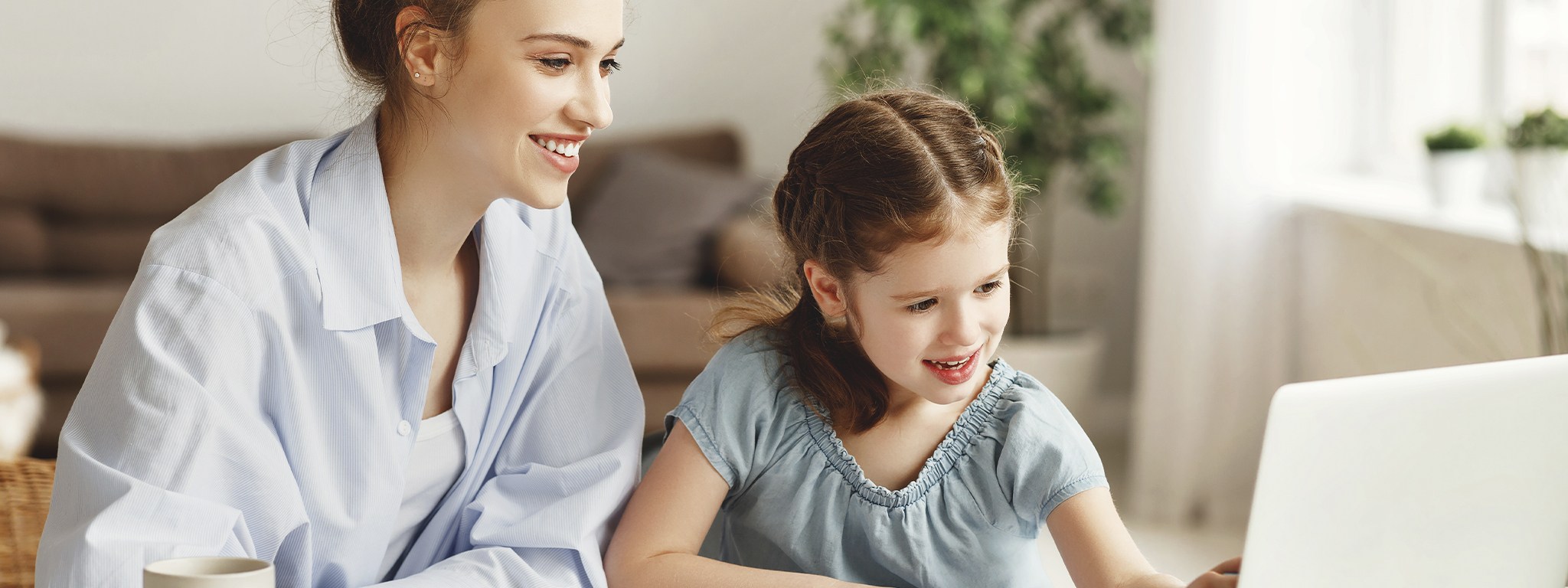 a woman helping her daughter searching for homework online sitting on a table with a laptop at home