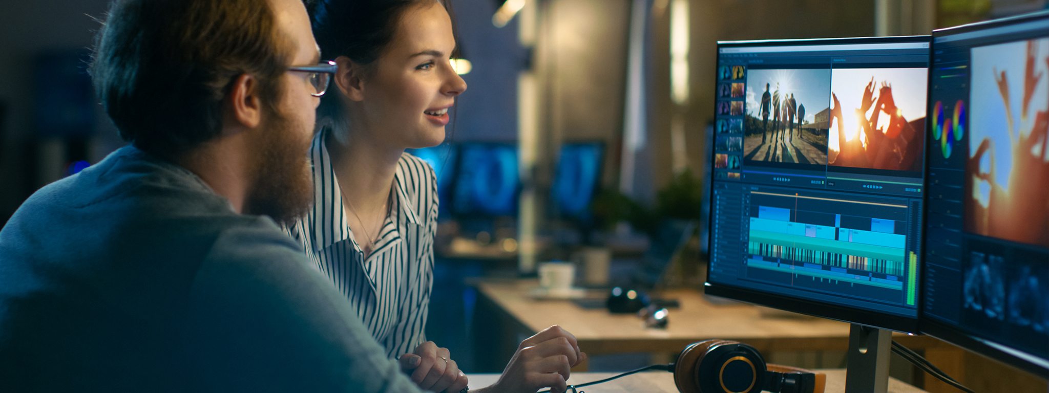 a man and a woman in an office editing a video on 2 monitors