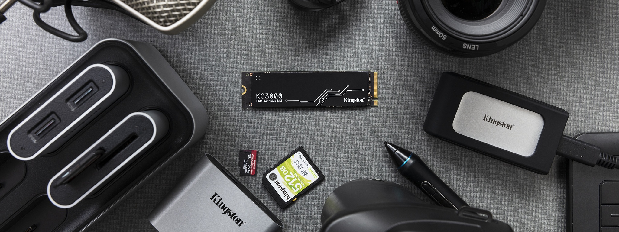 사진 촬영 장비와 함께 책상 위에 놓여 있는 Kingston 워크플로 스테이션, KC3000 NVMe SSD, XS2000 휴대용 SSD, SD 카드 및 마이크로SD 메모리 카드