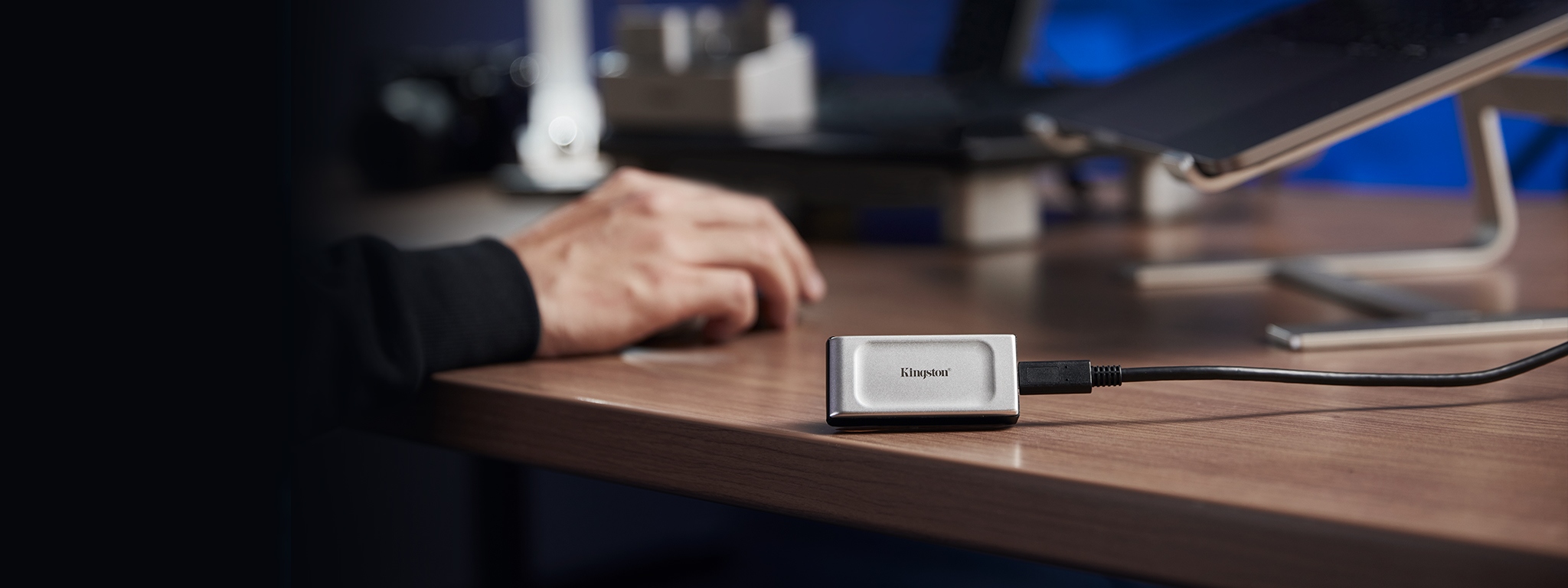 An XS2000 external SSD sits at the edge of a desk next to a laptop on a stand