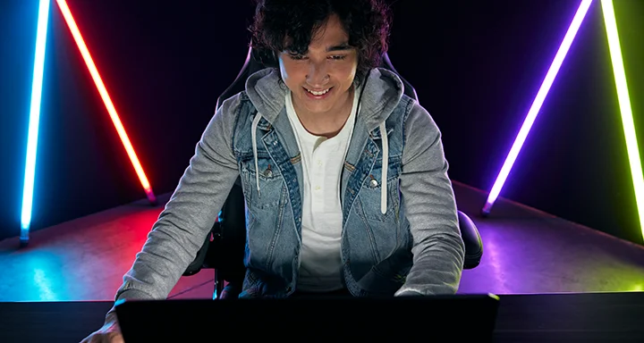 Um gamer sentado a uma mesa com luzes fluorescentes multicoloridas ao fundo.