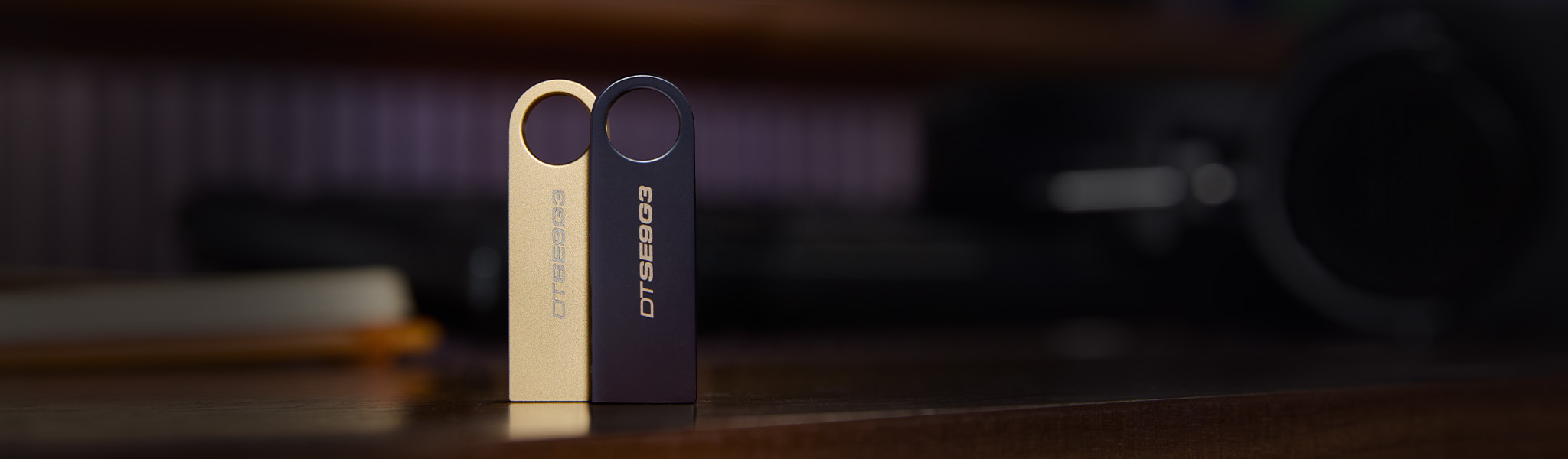 Dois drives DTSE9G3 USB em pé sobre uma mesa, um dourado e um em níquel.