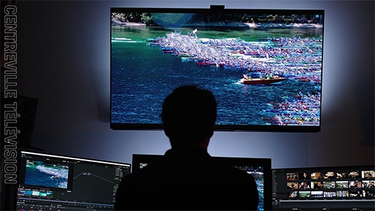 A silhouette of a video editor working with monitors and a larger screen displaying his project in a dimly lit room